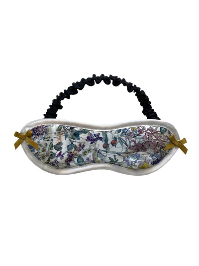 Liberty London silk eye mask with multicolored floral print, black silk lining, and gold ribbon bows